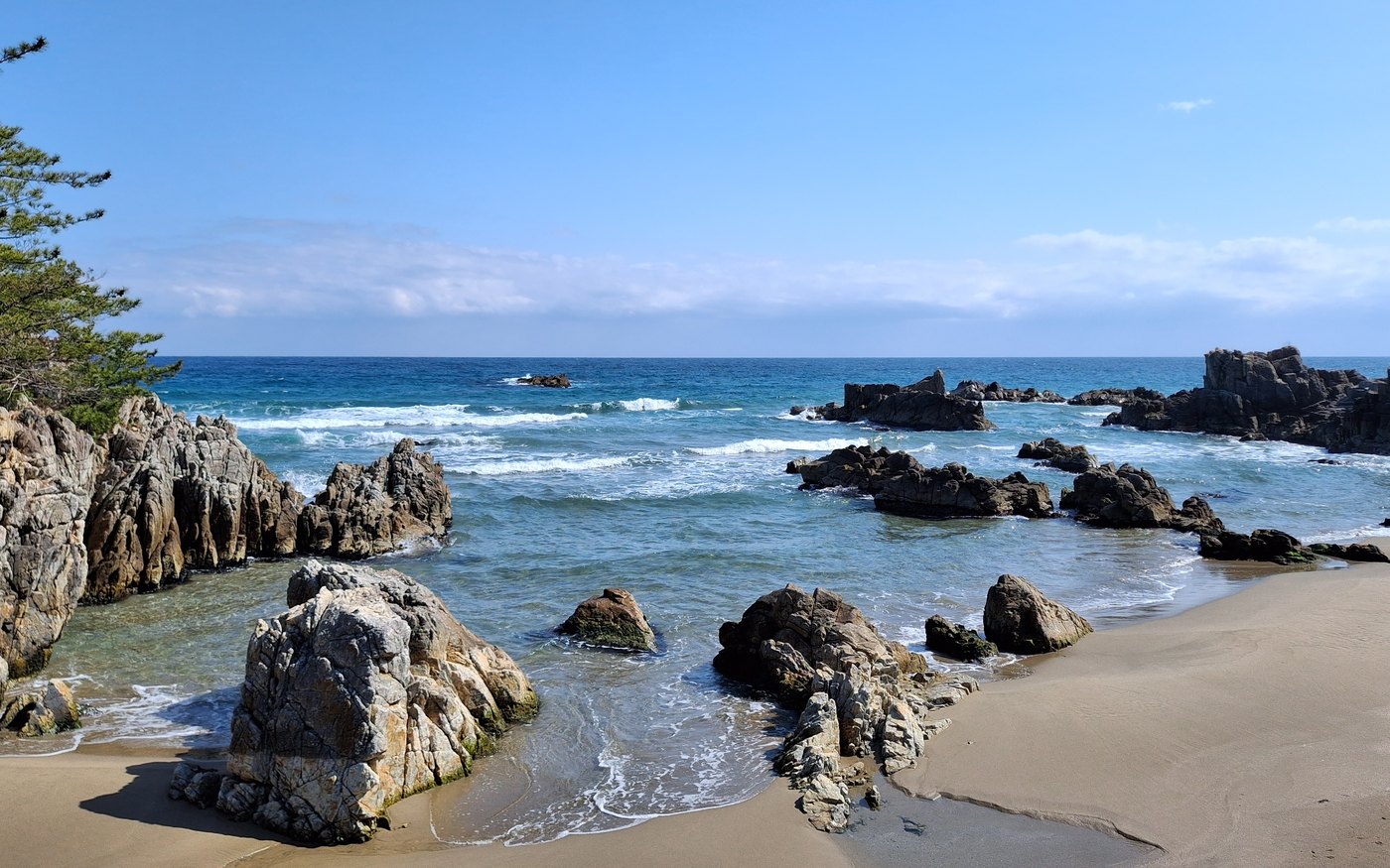 Rocks and a small sandy cove at Bunam Beach, with pine trees above the sea